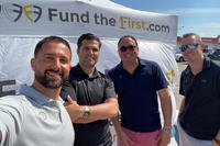 four men standing in front of the fund the first banner