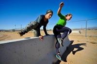 Nora Zazueta and Emily Lilo, members of Team CrossFit 623, leap over a barrier as part of the explosive ordnance disposal physical training challenge at Luke Air Force Base.