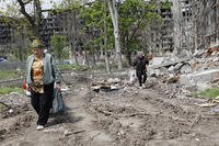 Women walk past a destroyed apartment building in Mariupol.