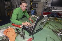 An aviation structural mechanic second class reads maintenance instructions on a laptop computer while conducting aircraft equipment maintenance aboard the amphibious assault ship USS Makin Island.