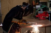 Staff Sgt. Natalie Delgado cuts a piece of equipment with her torch as sparks fly on the ground.