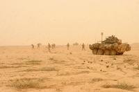 An armored vehicle and troops on foot in a dusty desert landscape.