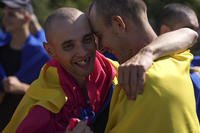 Ukrainian prisoners of war wrapped in national flags hug each other.