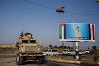 U.S. military vehicle passes by a poster of Syrian President Bashar Assad