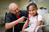 A nurse give a girl, who is looking into the camera, an injection in her arm.