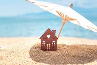 house cutout under paper umbrella in sand