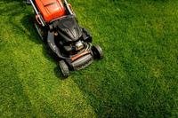 An orange and black lawn mower pictured from above crossing green grass.