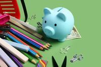 School supplies surround a blue piggy bank.