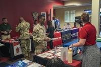 A U.S. airman talks to a college representative across a table of pamphlets.