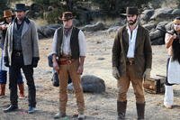 Three cowboys stand under guard in a rocky desert clearing as two Apache warriors hold them at gunpoint in the Western film “Frontier Crucible.”