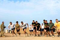 Service members in the desert, wearing PT uniforms, take off running.