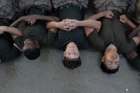 Marines pictured upside-down, lying in the sand linking arms.