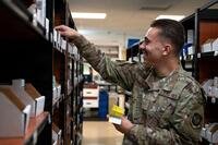 A pharmacy technician in an Air Force uniform stocks a pharmacy shelf.