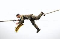 A soldier on a rope unhooks a sign representing a ranger tab.