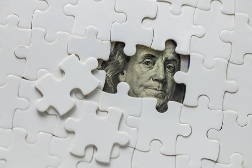 Through a two-piece gap in a blank white jigsaw puzzle looks the face of a U.S. president on a bill.