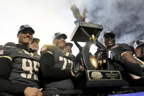 Army players hoist the winner's trophy after a football game.