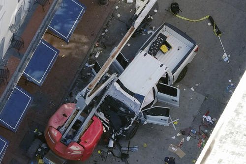 A black flag with white lettering lies on the ground rolled up behind a pickup truck