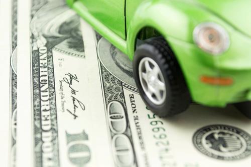 A green toy car rolls over $100 bills.