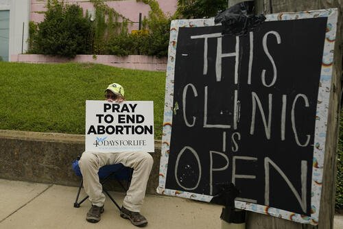 FILE - An anti-abortion supporter sits behind a sign that advises the Jackson Women's Health Organization clinic is still open in Jackson, Miss., July 6, 2022. (AP Photo/Rogelio V. Solis, File)